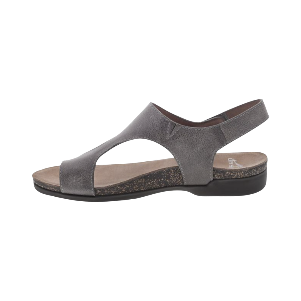Dansko Women’s Reece Sandal in Stone Waxy featuring a genuine leather upper, minimalist open-toe silhouette, adjustable hook-and-loop strap, Dansko Natural Arch® technology, molded EVA footbed, lightweight rubber outsole, and supportive design built for lasting comfort and everyday wear.