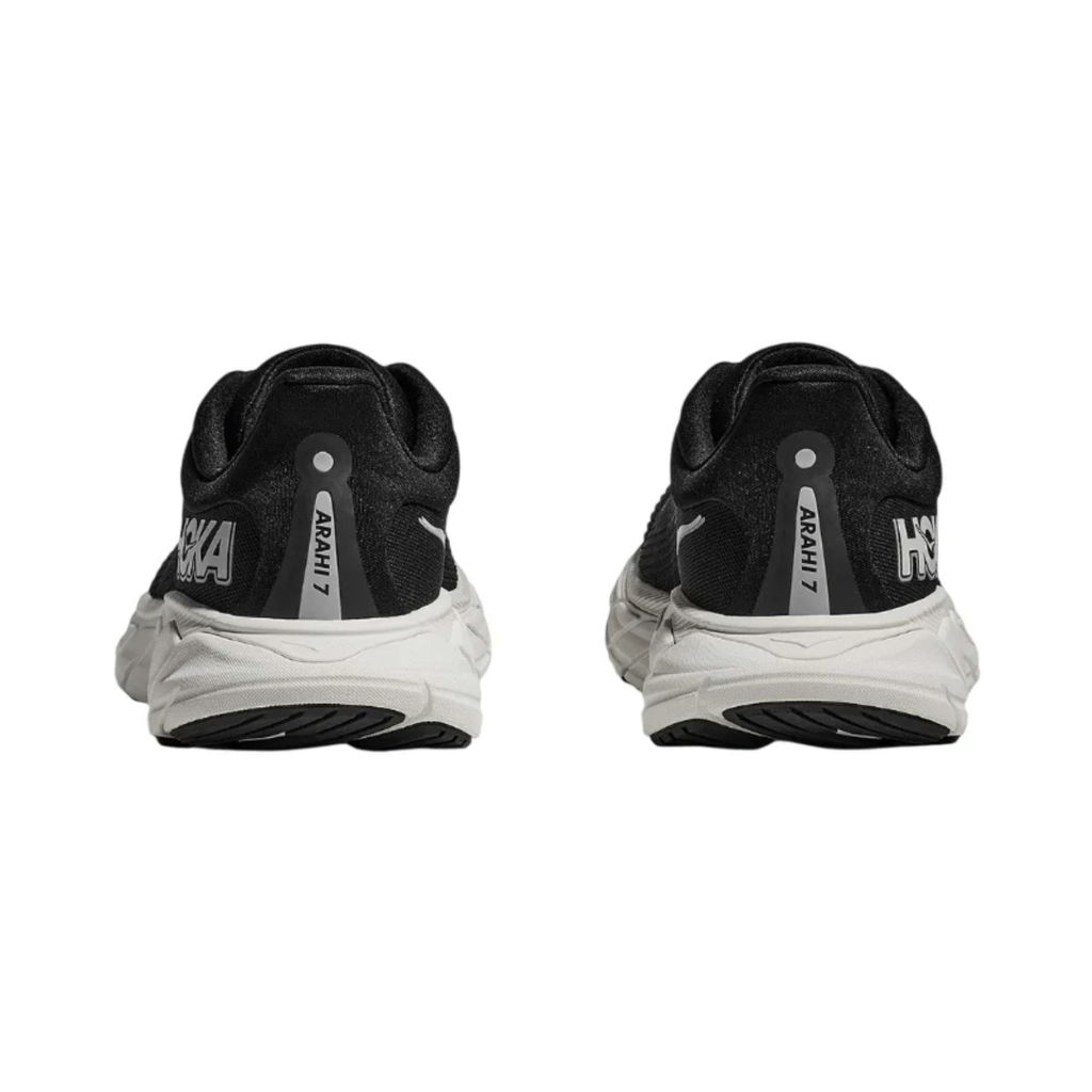 Rear view of the Women's HOKA Arahi 7 in Black/White highlighting the plush heel collar, J-Frame™ stability system, cushioned heel, and durable rubber outsole for reliable support and traction.